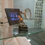 book, magnifying glass, digital image display and plastic hand in glass display case