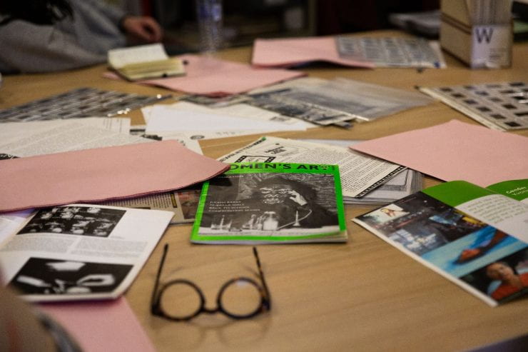 magazines, newsprint publications and slide files spread across a table with a pair of researcher's glasses.