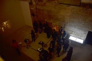 group of people seen from above in a darkened space watching a speaker and a slide projection