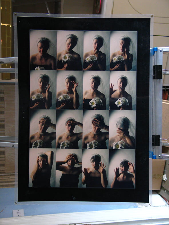 Photograph of a grid of four by four photos each showing a white woman dressed as bride holding flowers and wearing a veil. The photographs have been laminated and are propped up against a domestic appliance.