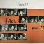 Horizontal photograph of strips of black and white negatives of of photos of a white dark haired woman with glasses, stuck on an orange cardboard folder with faded masking tape