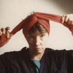 Photographic portrait of middle-aged white woman tying a red scarf to her head
