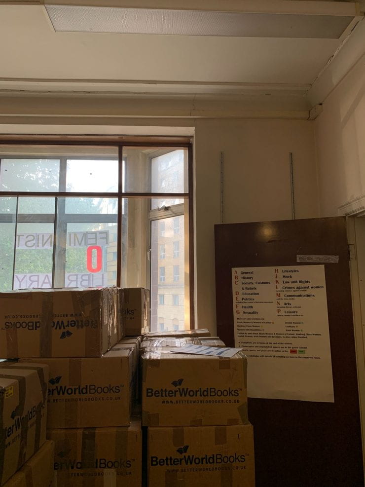 A room full of boxes of books, the words feminist library are seen in the window