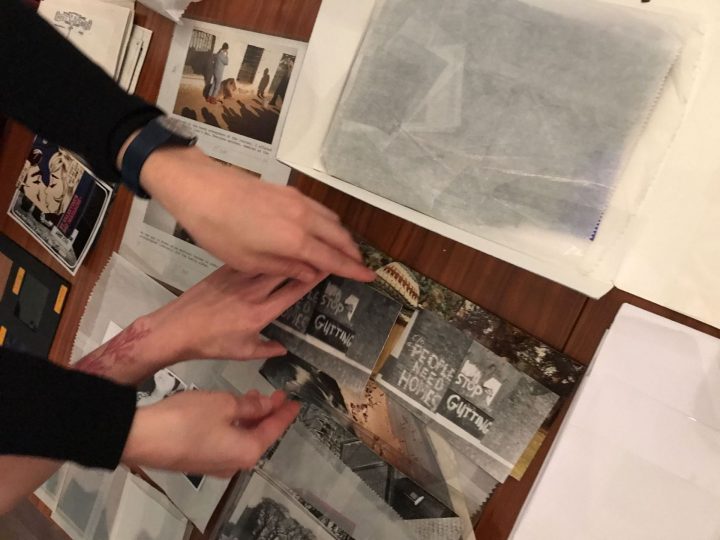 Two people's hands move photographs on a table on which many different colour and black and white photographs have been laid out. 