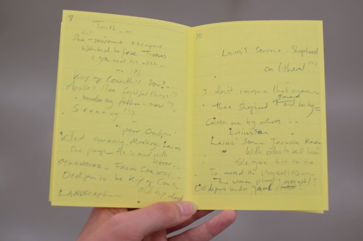 A small bright yellow booklet is held open on a double page spread, both sides filled with handwritten notes.