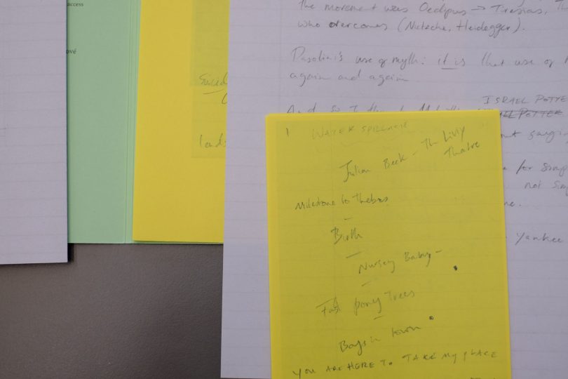 On a table, yellow, white and light green papers with handwritten notes are spread out, overlapping so the ones underneath can just be seen.