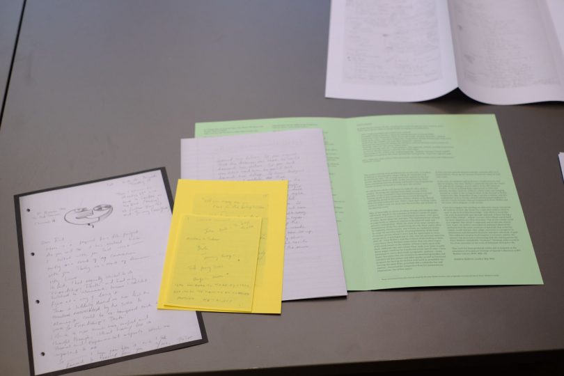 On a table, yellow, white and light green paper booklets with handwritten notes are spread out, overlapping so the ones underneath can just be seen.