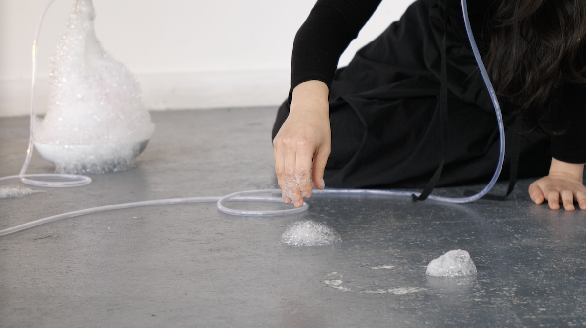 A person performing with tubes and bubbles on a grey floor.