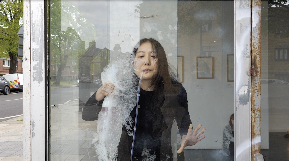 A person performing with tubes and bubbles against a window.
