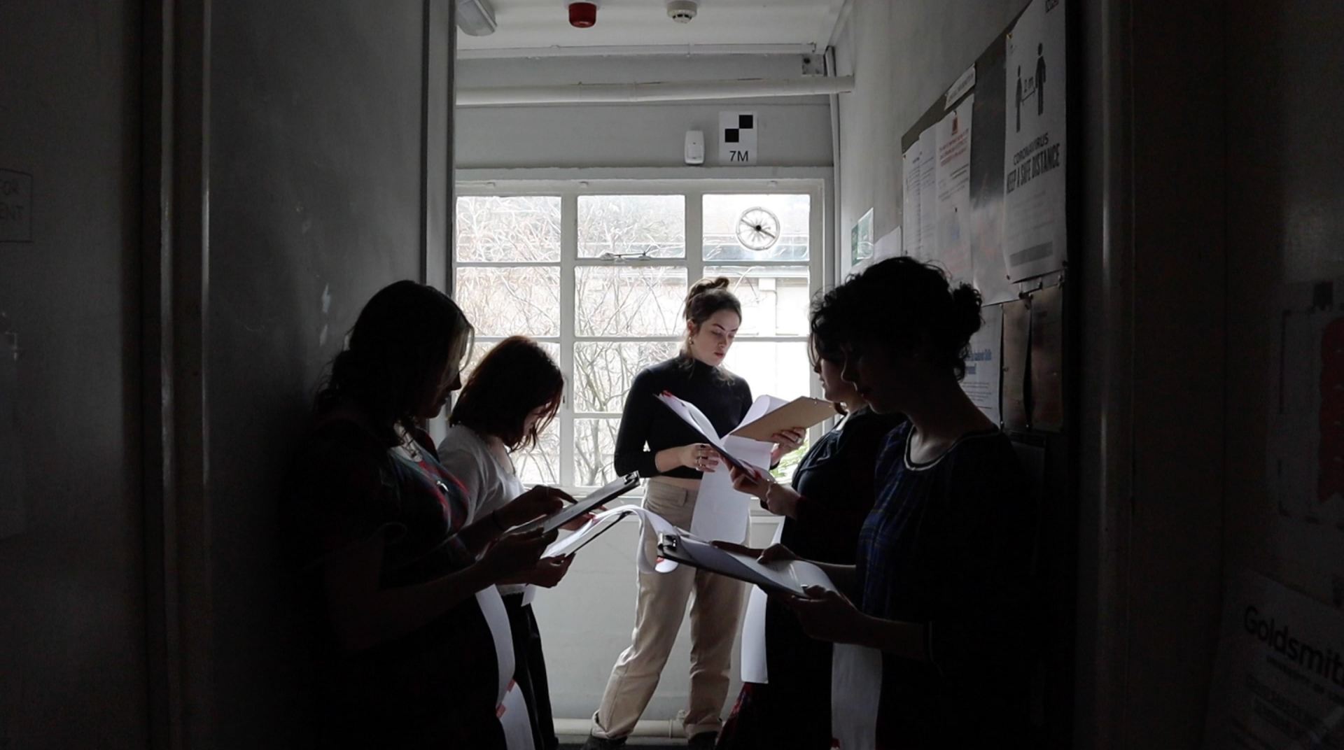 A photo of several people standing in a hallway reading a script.