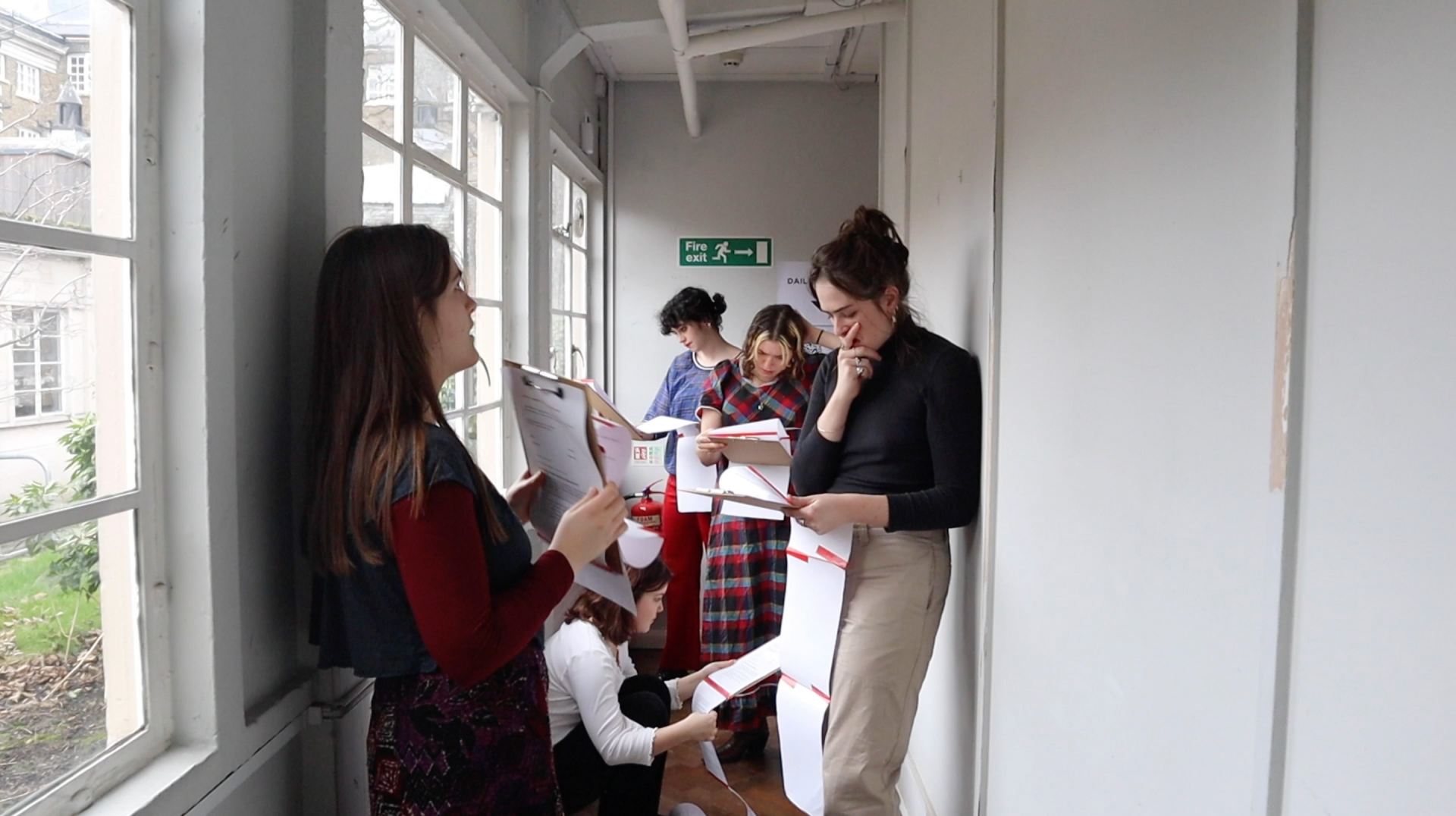 A photo of several people standing in a hallway reading a script.