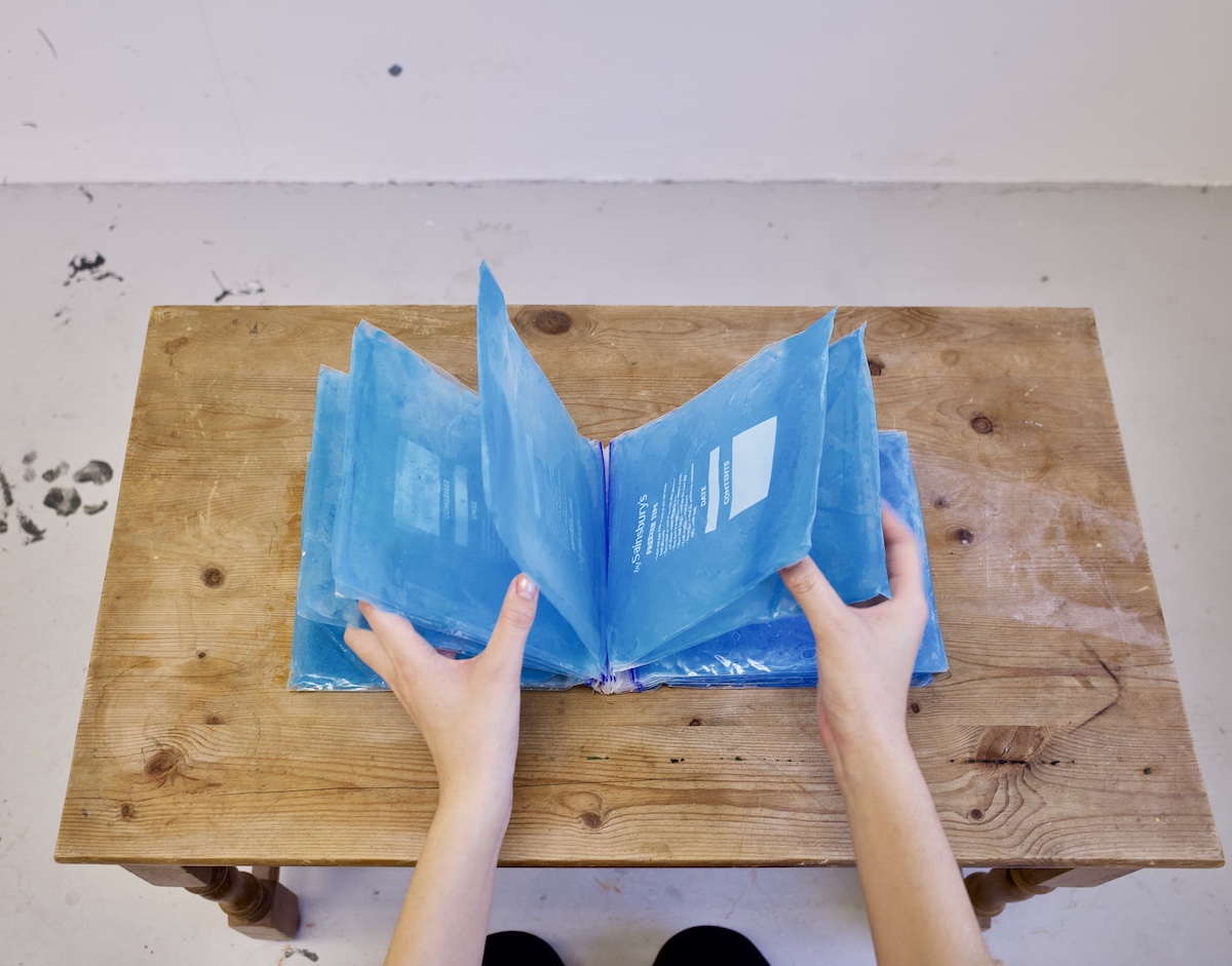 An image of a person's hands leafing through a book made out of frozen bags of ice.