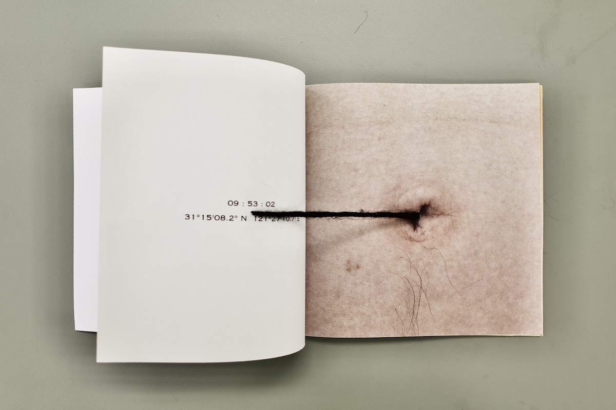 a image of a book from above. the left hand page is pulling a black string from an image of a belly button on the right hand page.