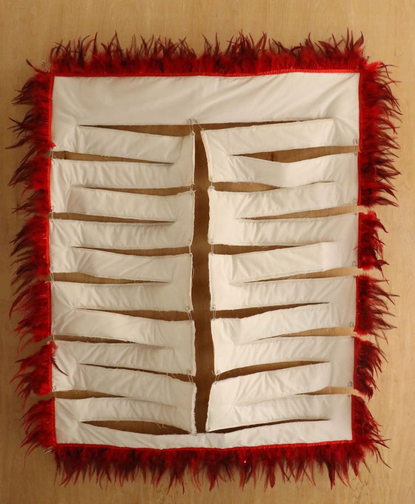 A white, bisected textile rectangle with a fluffy, red trim around the edge.