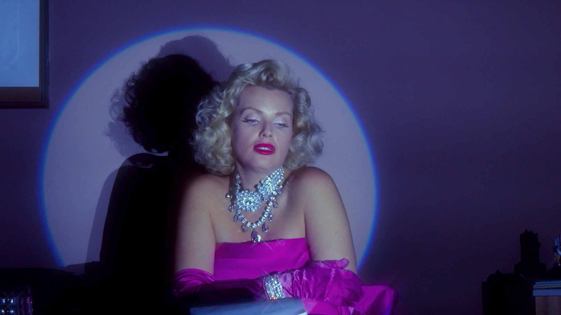 A Marilyn Monroe impersonator sits in a spotlight.  