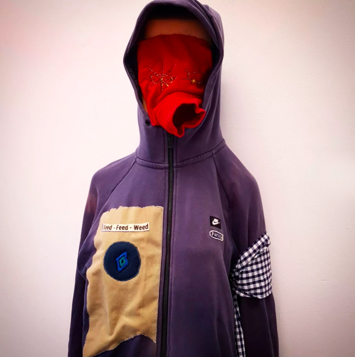 A mannequin in an embroidered purple hoodie and red balaclava.