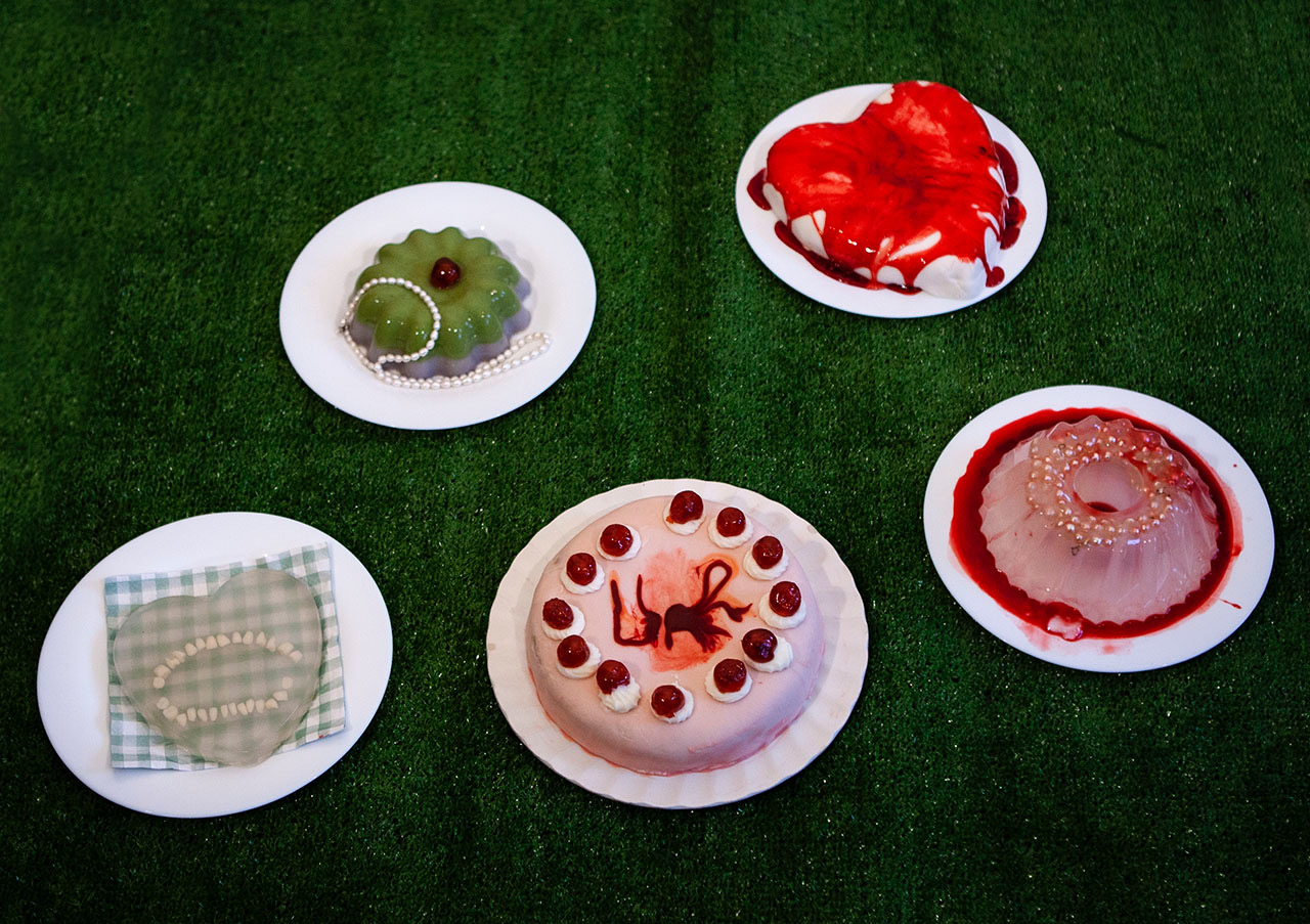 A sculptural picnic scene including two jelly sculptures and two cakes with take blood and teeth. 