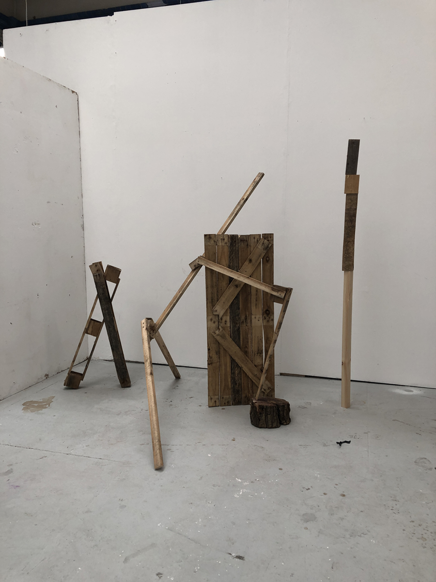A series of three wooden sculptures made from pallet wood and nails standing in a white-walled room.
