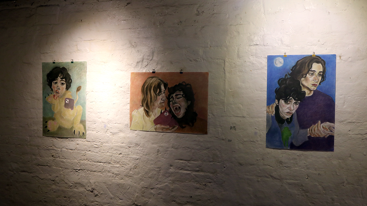 A set of three spotlit paintings hanging in a line on a white wall. 