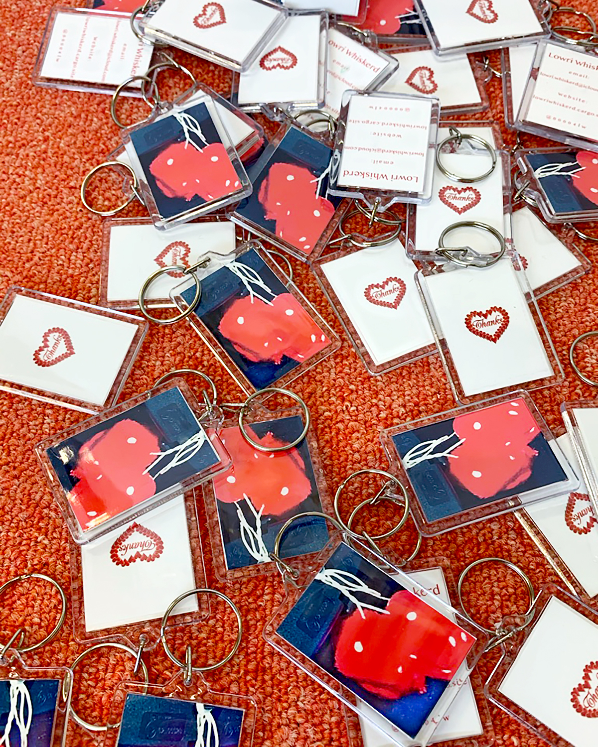 Several keyrings containing images of love-hearts are scattered across a red carpet. 