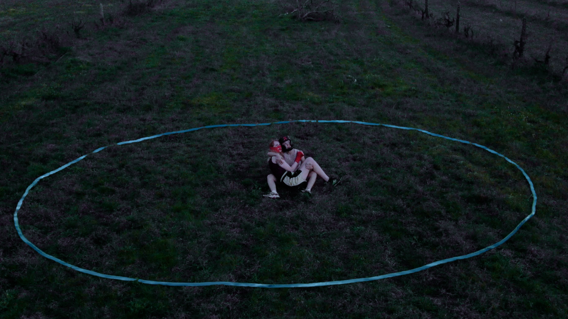 Two people embrace within a stone circle in a field.