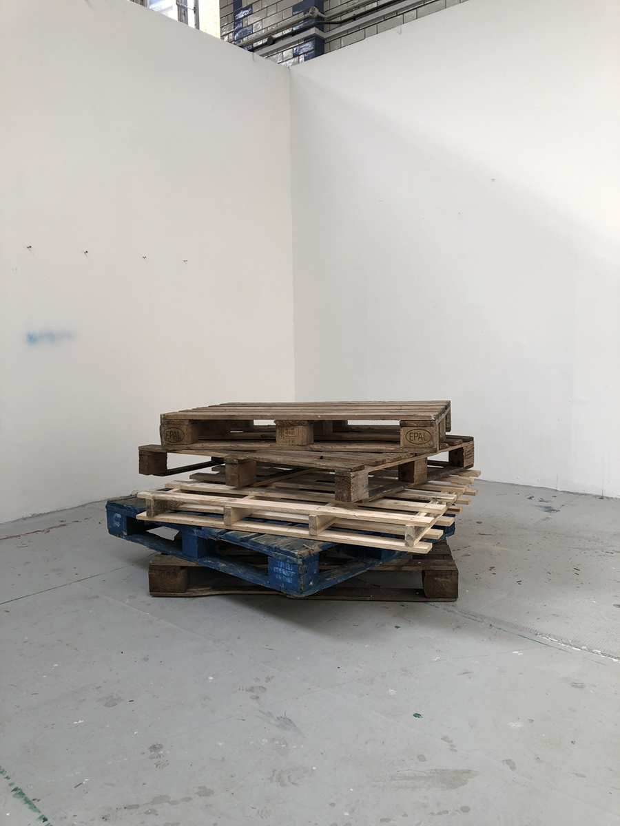 Five wooden pallets stacked on top of one another, featuring four linear wooden sculptures.