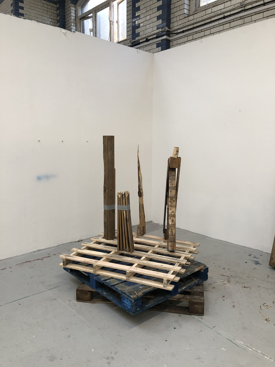 Five wooden pallets stacked on top of one another, featuring four linear wooden sculptures.