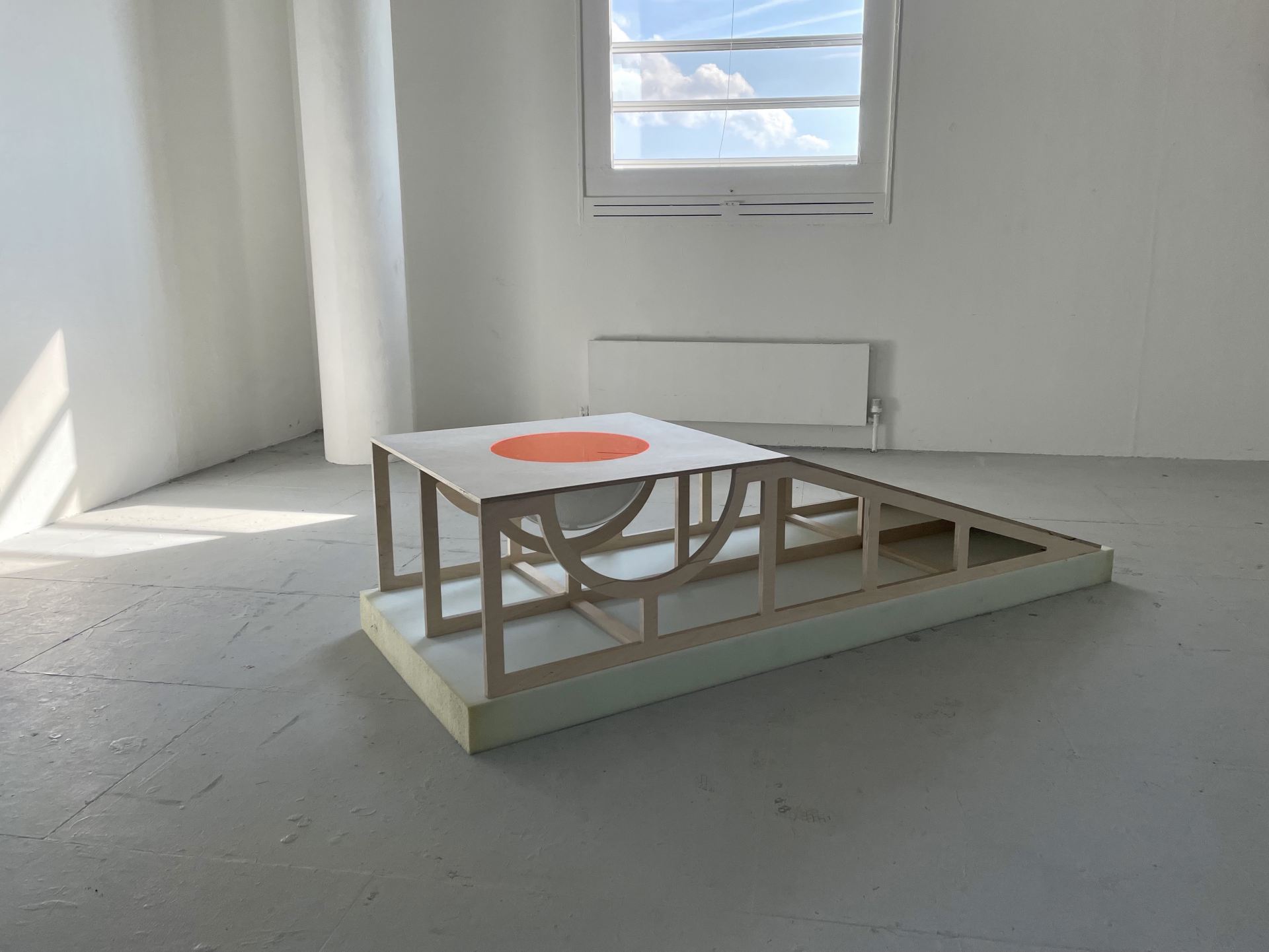 A sculpture of a wooden table-like object with a ramp standing in a room.