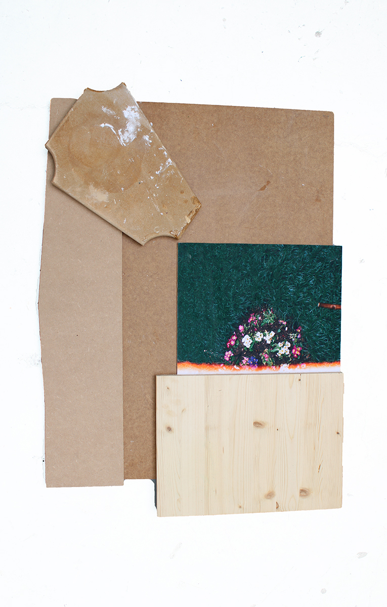 A collage made from wood, cardboard and fabric hanging on a white wall.
