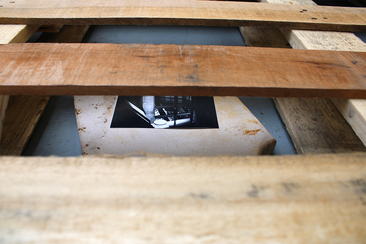 A view looking between the slats of a wooden pallet, showing a black and white photograph underneath.