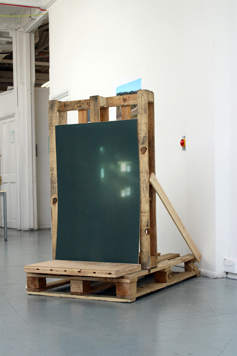 A sculpture made from wooden pallets and green plastic standing in a room.