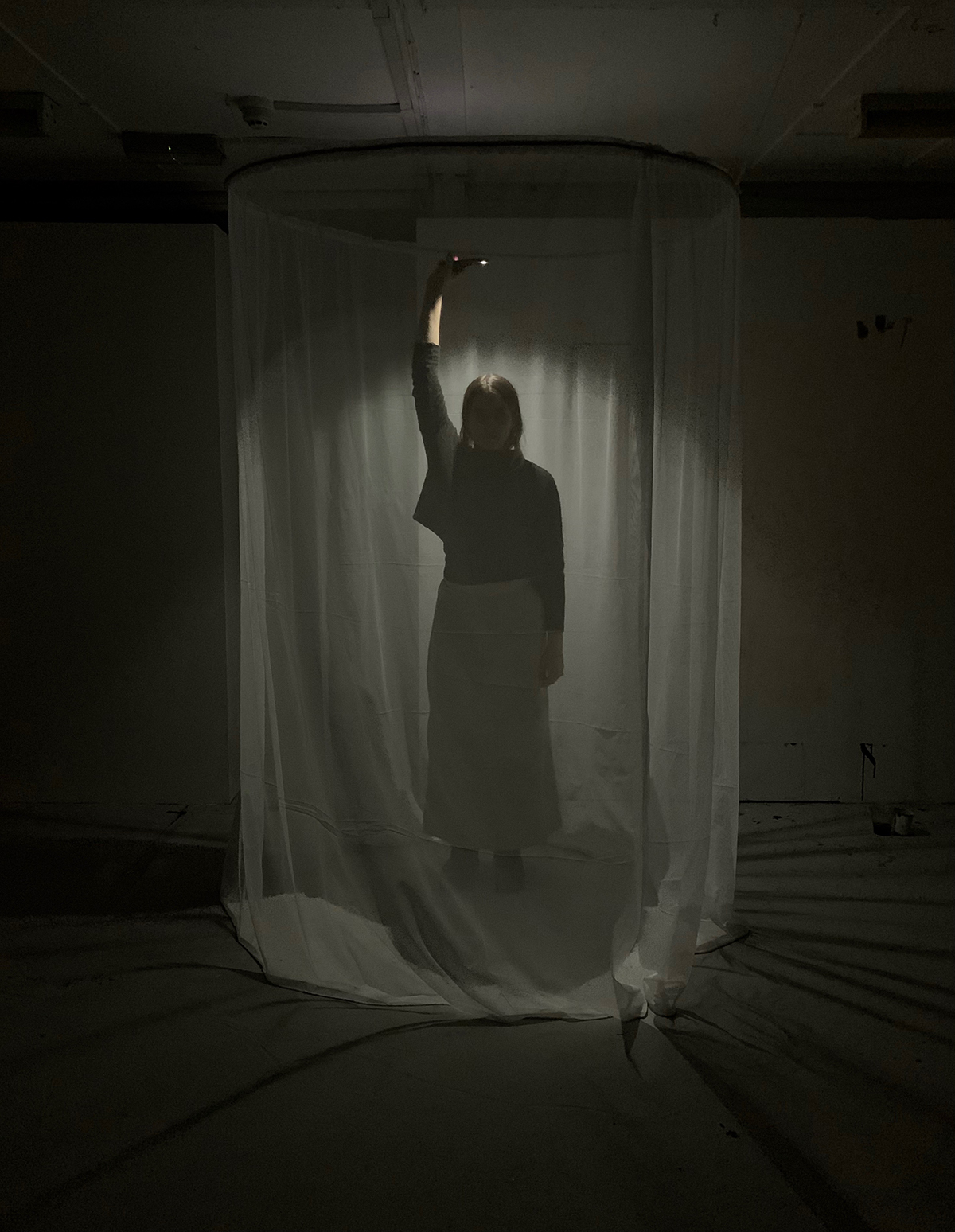 A figure stands in a circle of fabric hanging from the ceiling.