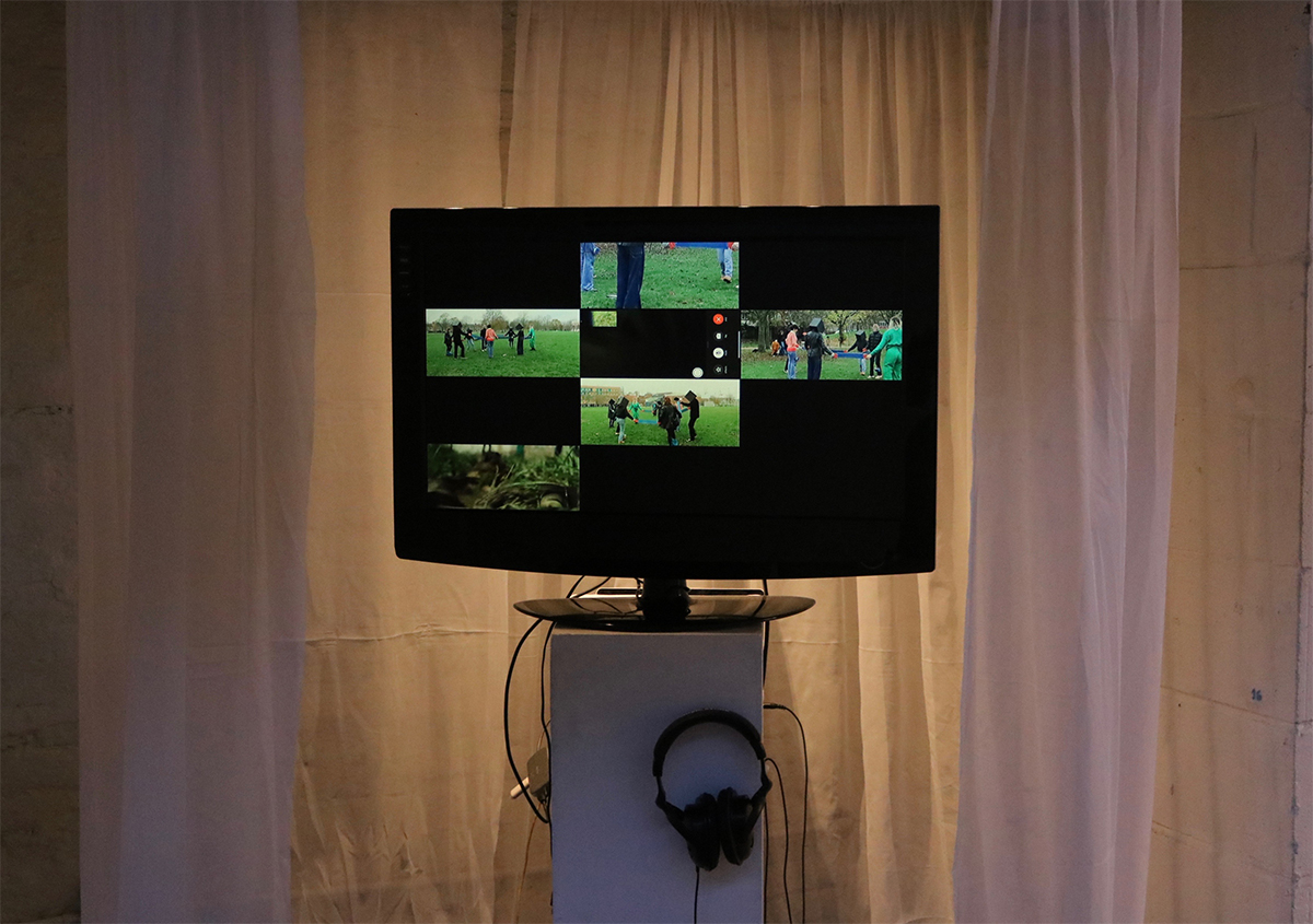 A tv stands against a fabric background, displaying several films of people in a field.
