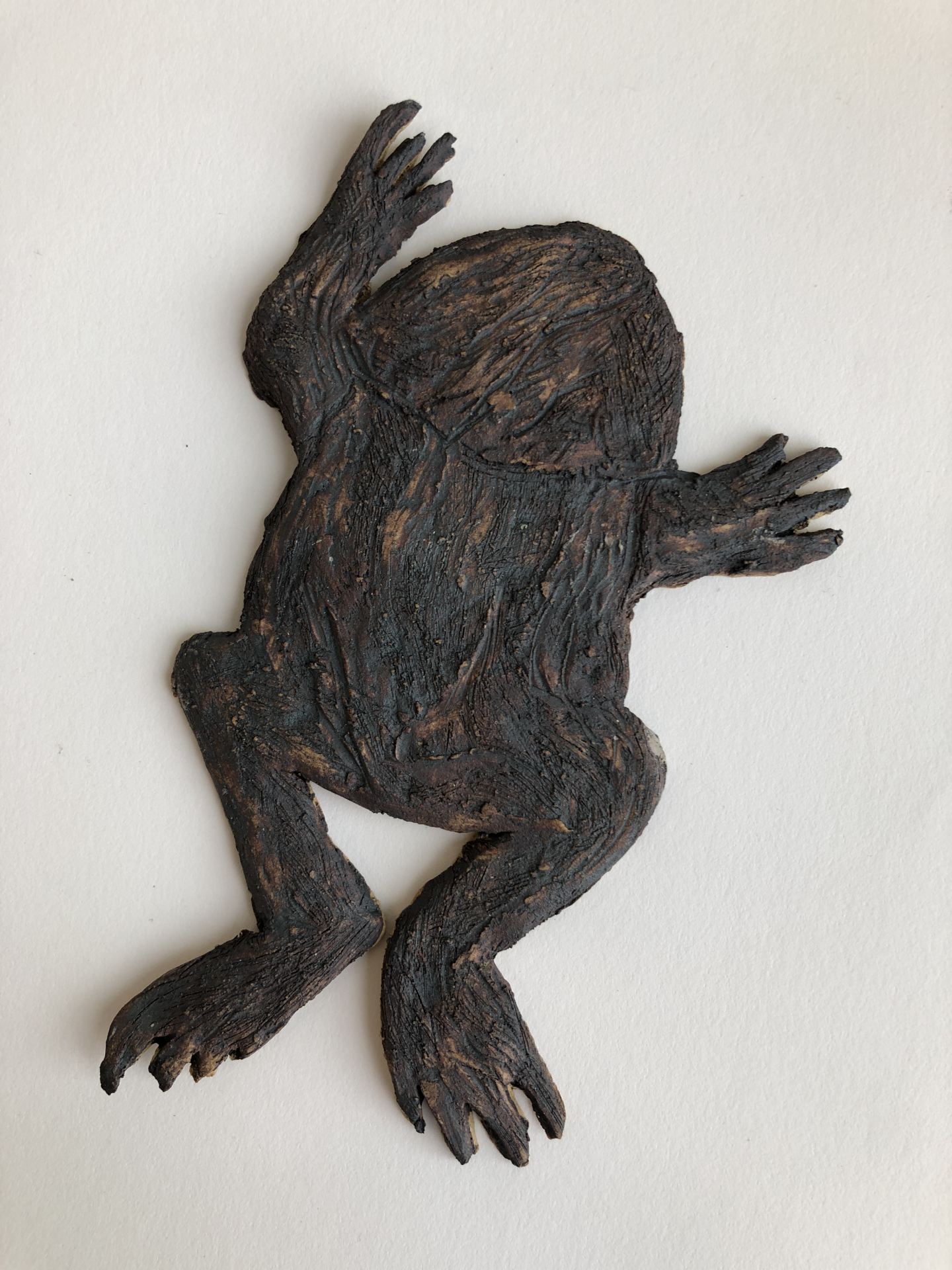 A brown  ceramic frog hangs on a wall.