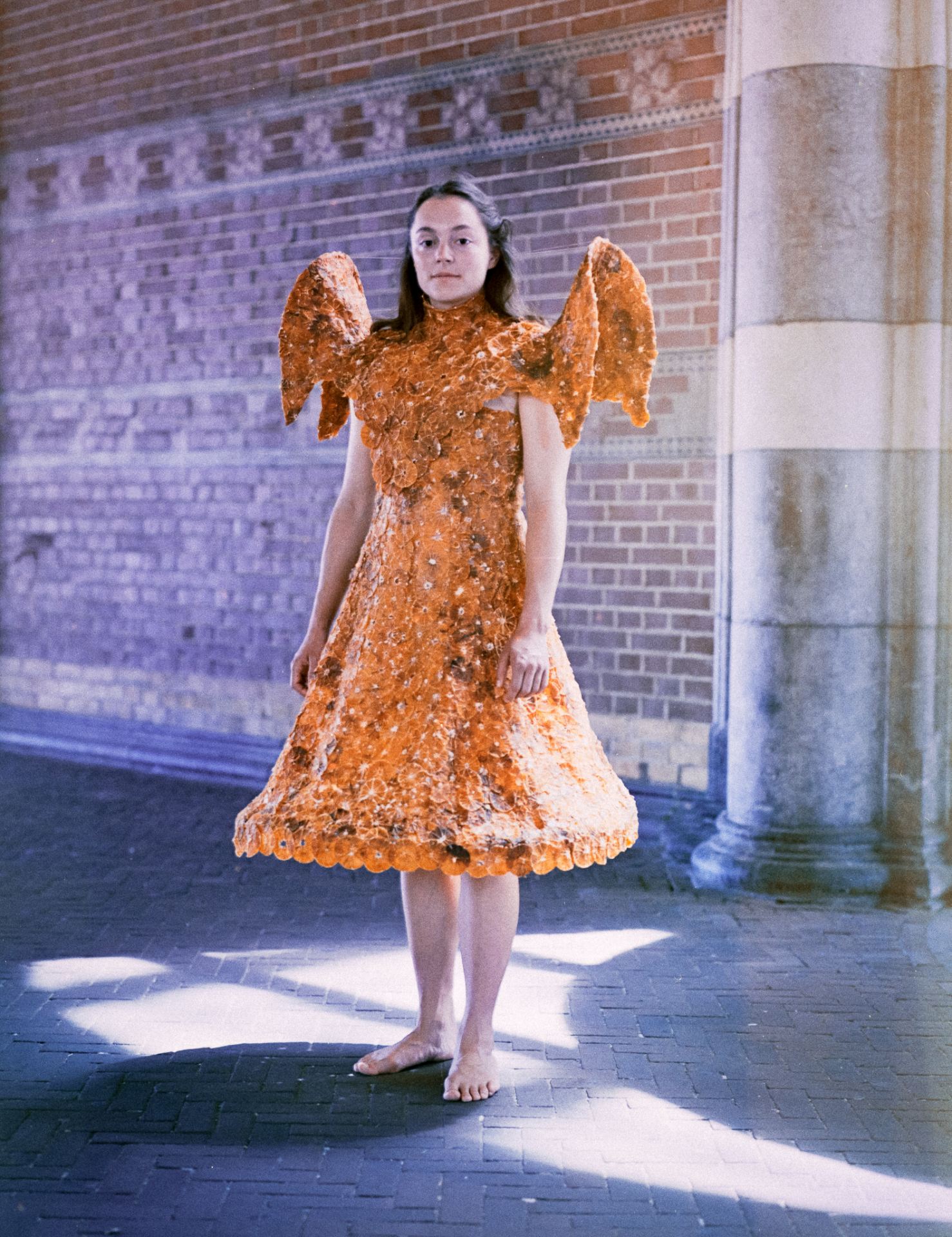A person stands in an angel-shaped dress made of 280 dried oranges.