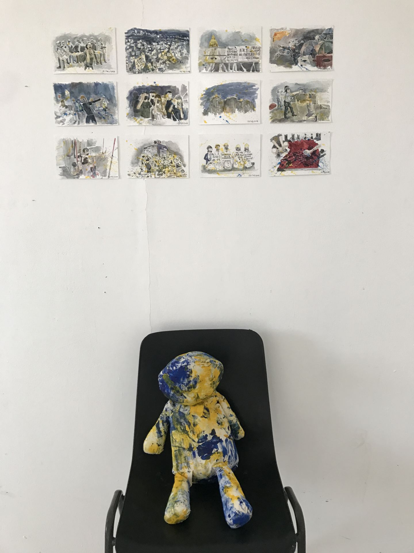 A paint-splattered teddy sits on a chair beneath 12 watercolour paintings.