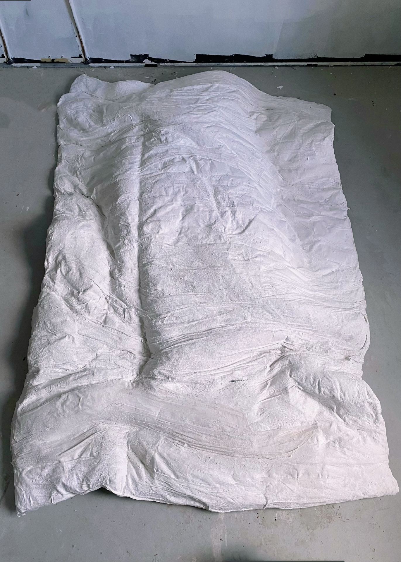 A piece of plaster cast to look like a duvet lying on a grey floor.