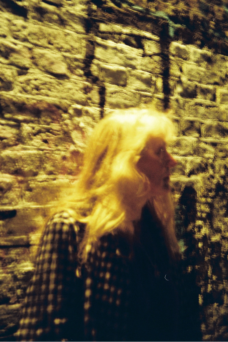 A photograph of a dimly lit person against a brick wall.