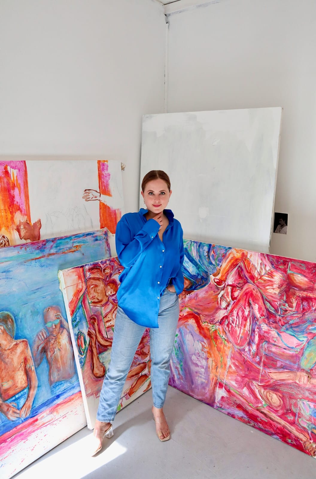 An image of a person in a blue shirt standing in front of some paintings in a studio.