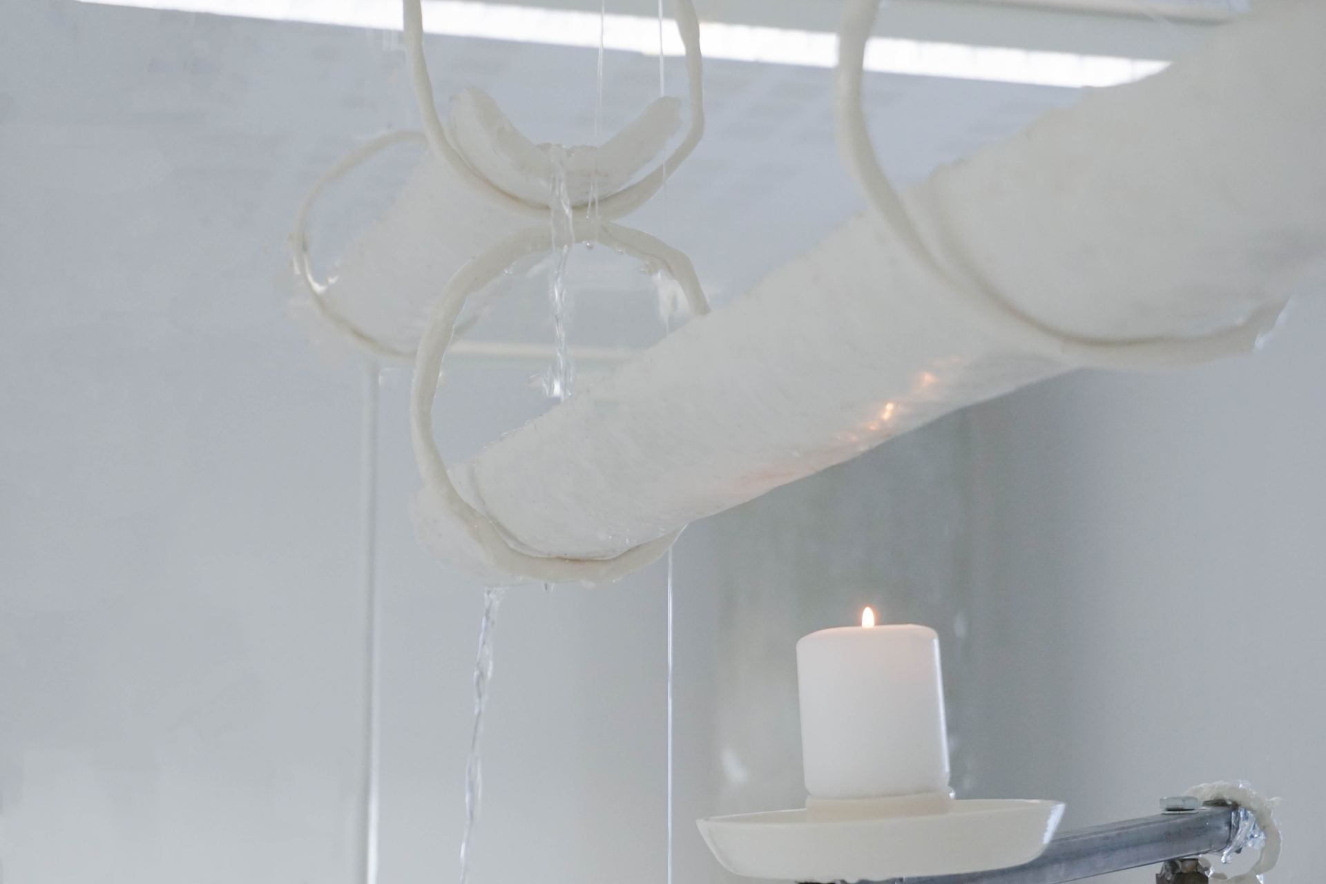 A detail shot of a sculptural water feature made using wax tubes standing in a white room.