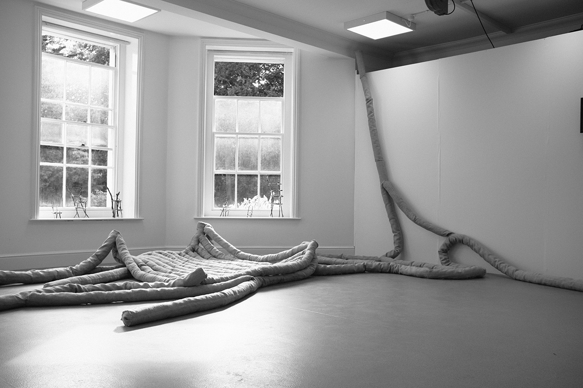 A fabric sculpture in a large white room, shot in greyscale.