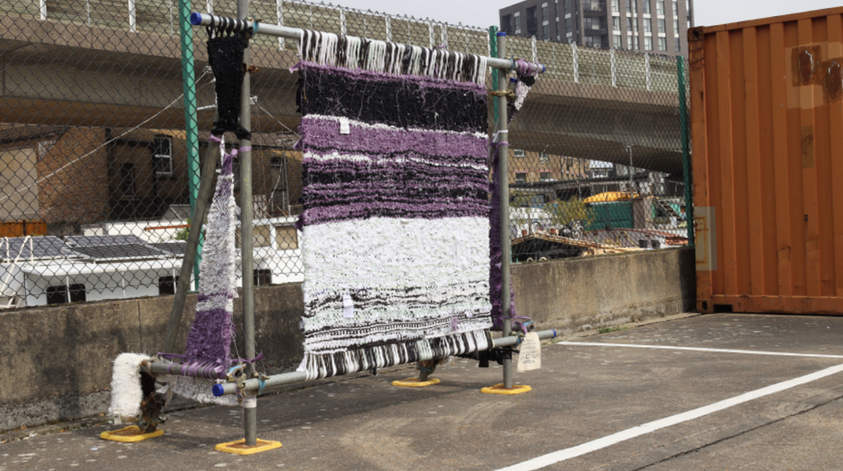 An abstract purple, white and black sculpture made of woven fabric stands near a dock.