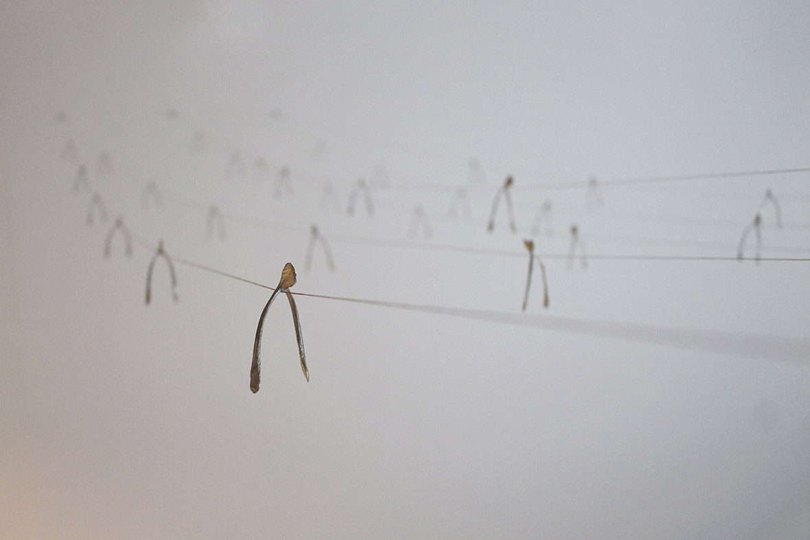 An image of several pewter wishbones hanging on wires in a white room.