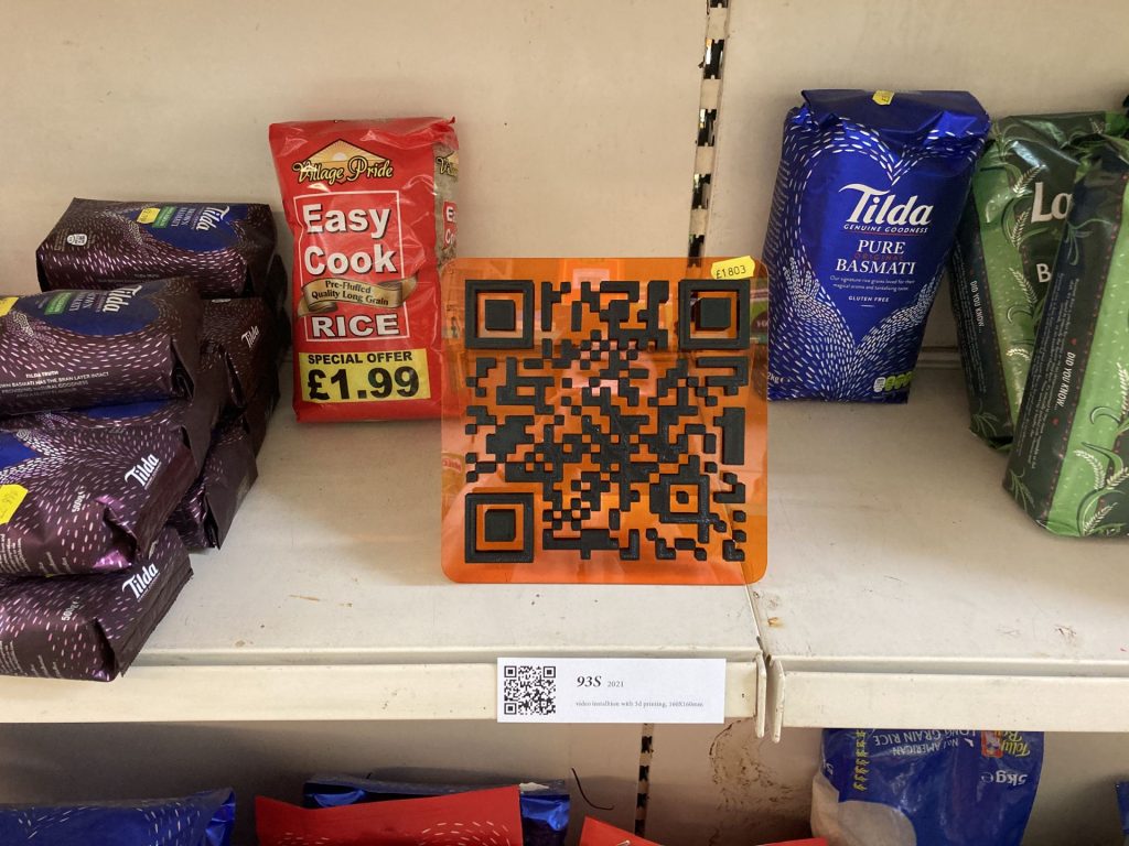 A 3D sculpture of a barcode installed on a shelf in a corner shop.