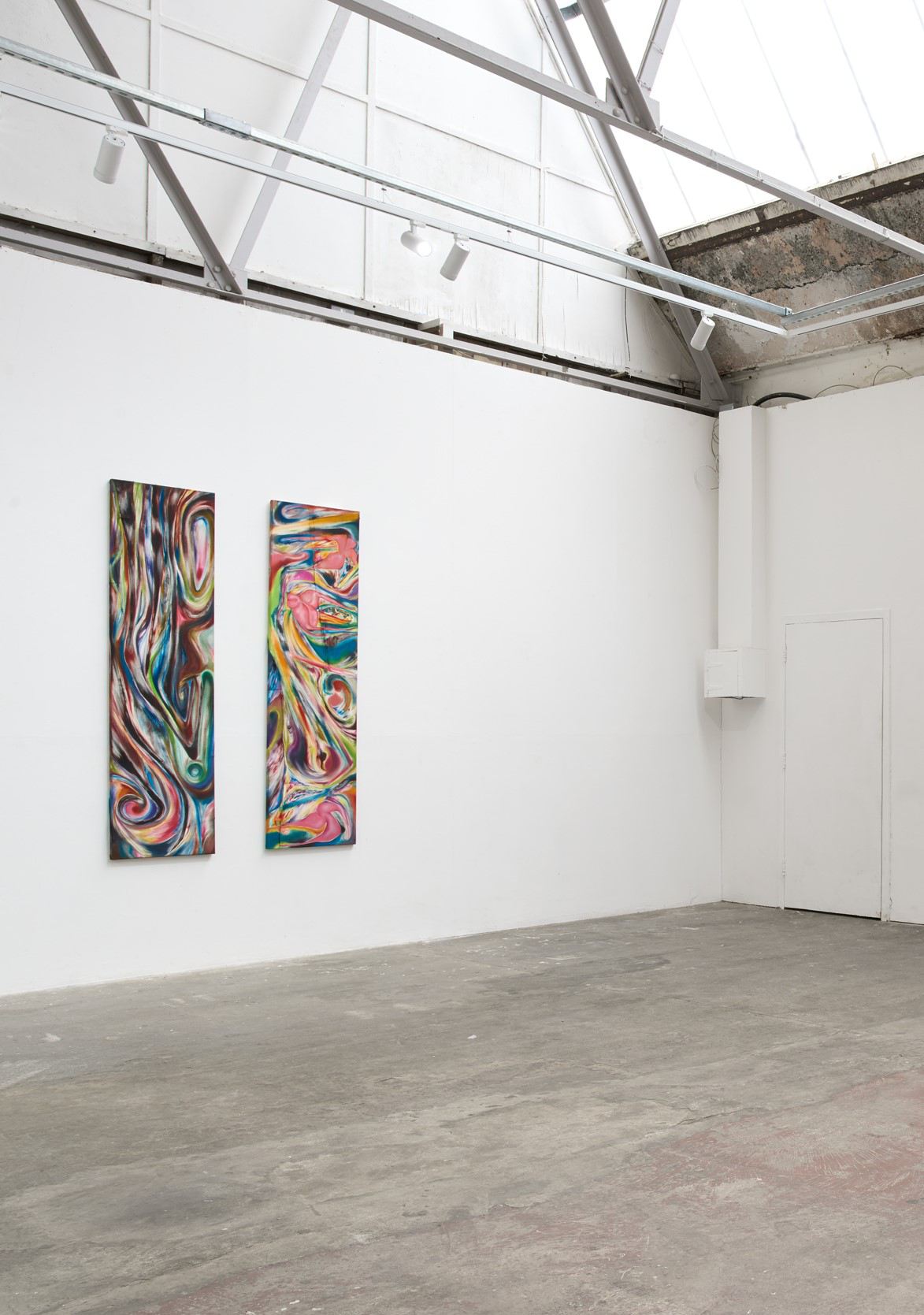 Two multicoloured paintings hanging in a white room.