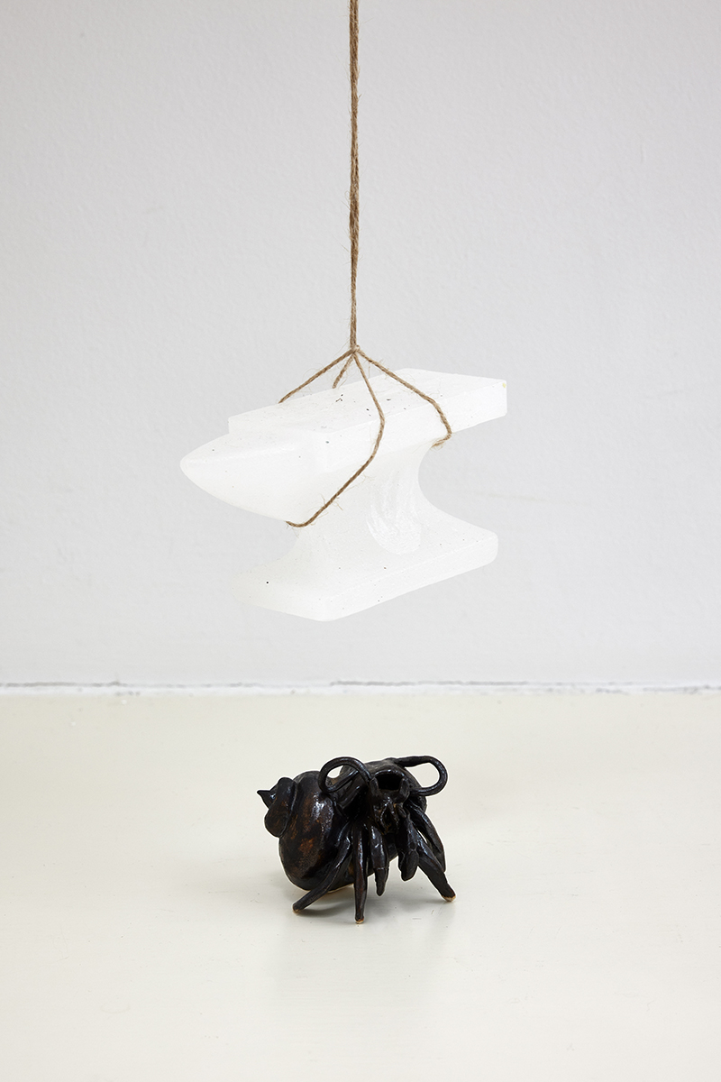 A sculpture of a Black ceramic hermit crab sat below a white ceramic anvil hanging from some string.