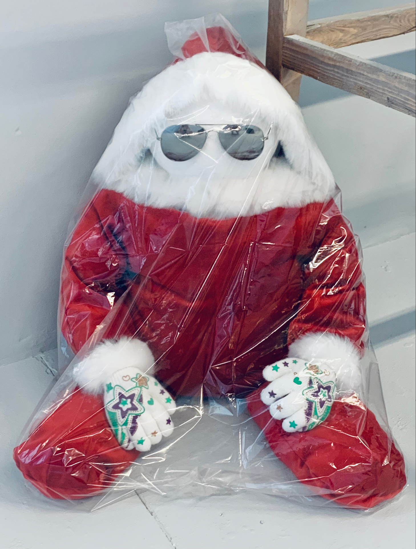 A photo of a small santa doll in silver aviators and wrapped in a clear dust sheet.