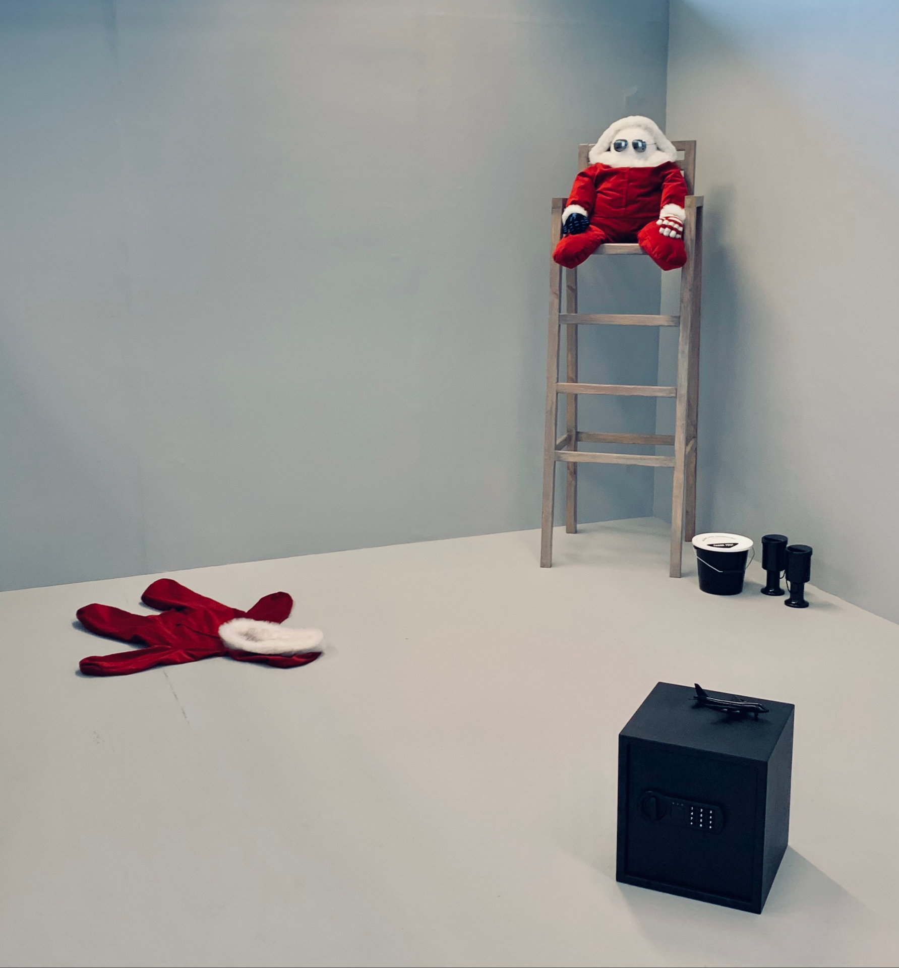 An image of an installation with a black safe, an empty santa baby grow and a small santa doll sat in a high wooden chair.