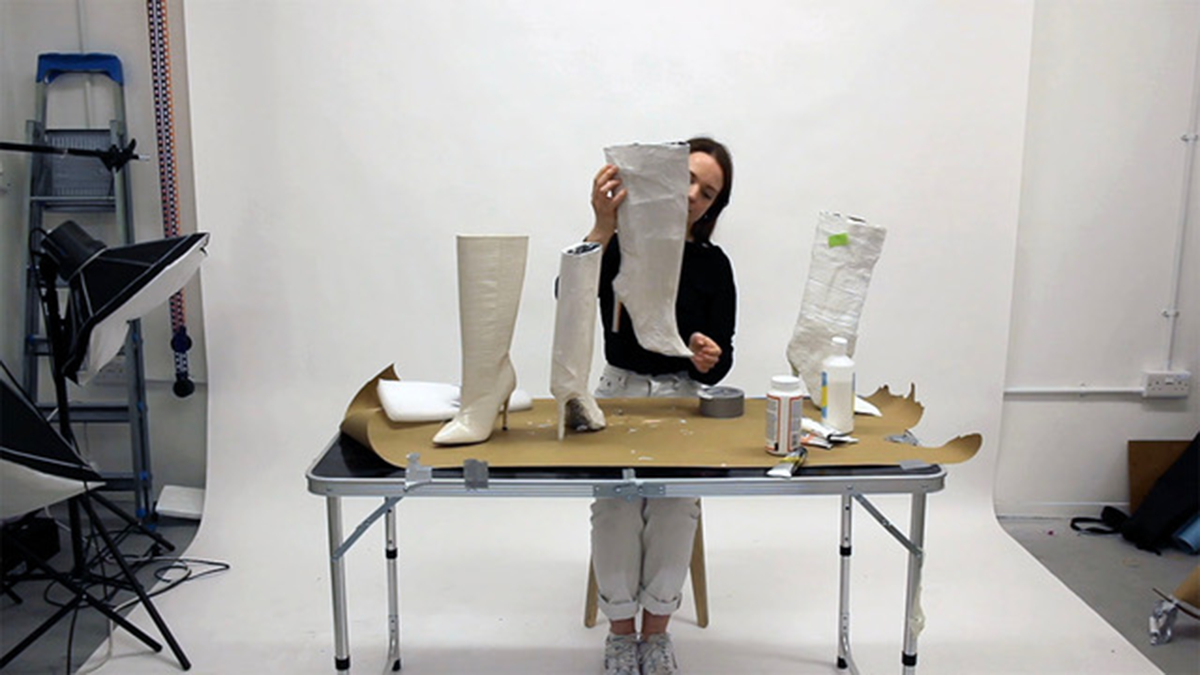 A video still of a person coating high-heeled boots in paper-mache.