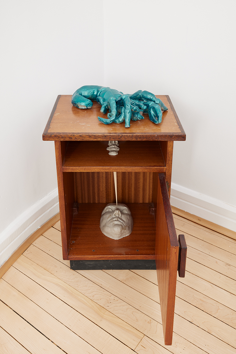 A sculpture of a blue hermit crab on a bedside table with a cast of a face inside.
